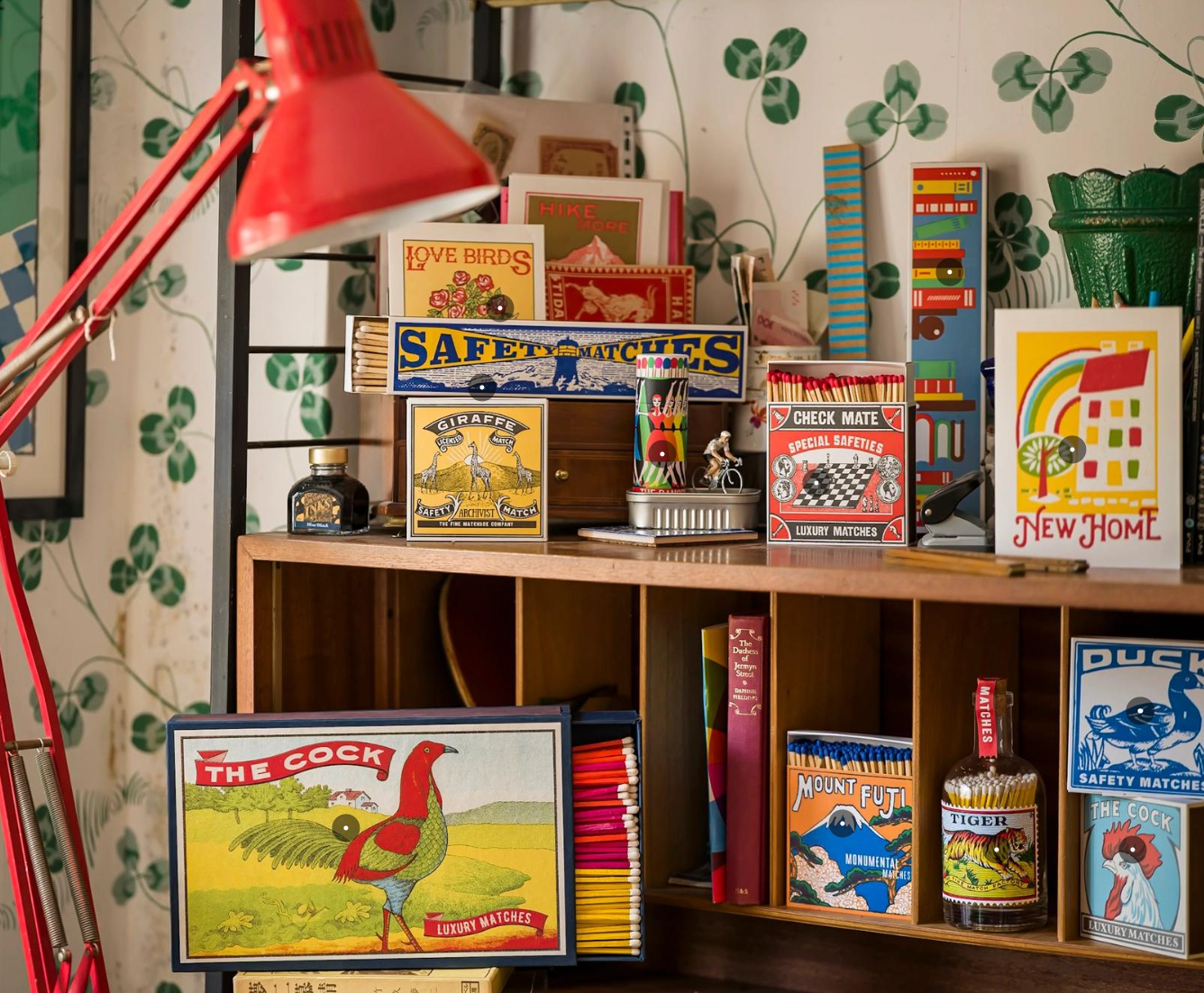 Collection of vintage matchboxes and books on a wooden shelf with a red lamp.