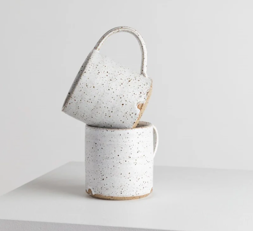 two white textured hand made mugs stacked on a white plinth