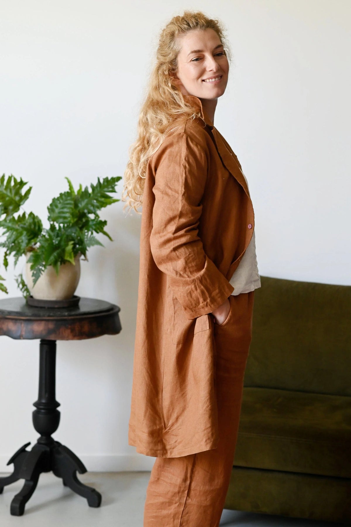 Woman wearing a brown outfit standing in a room with a plant and a couch.