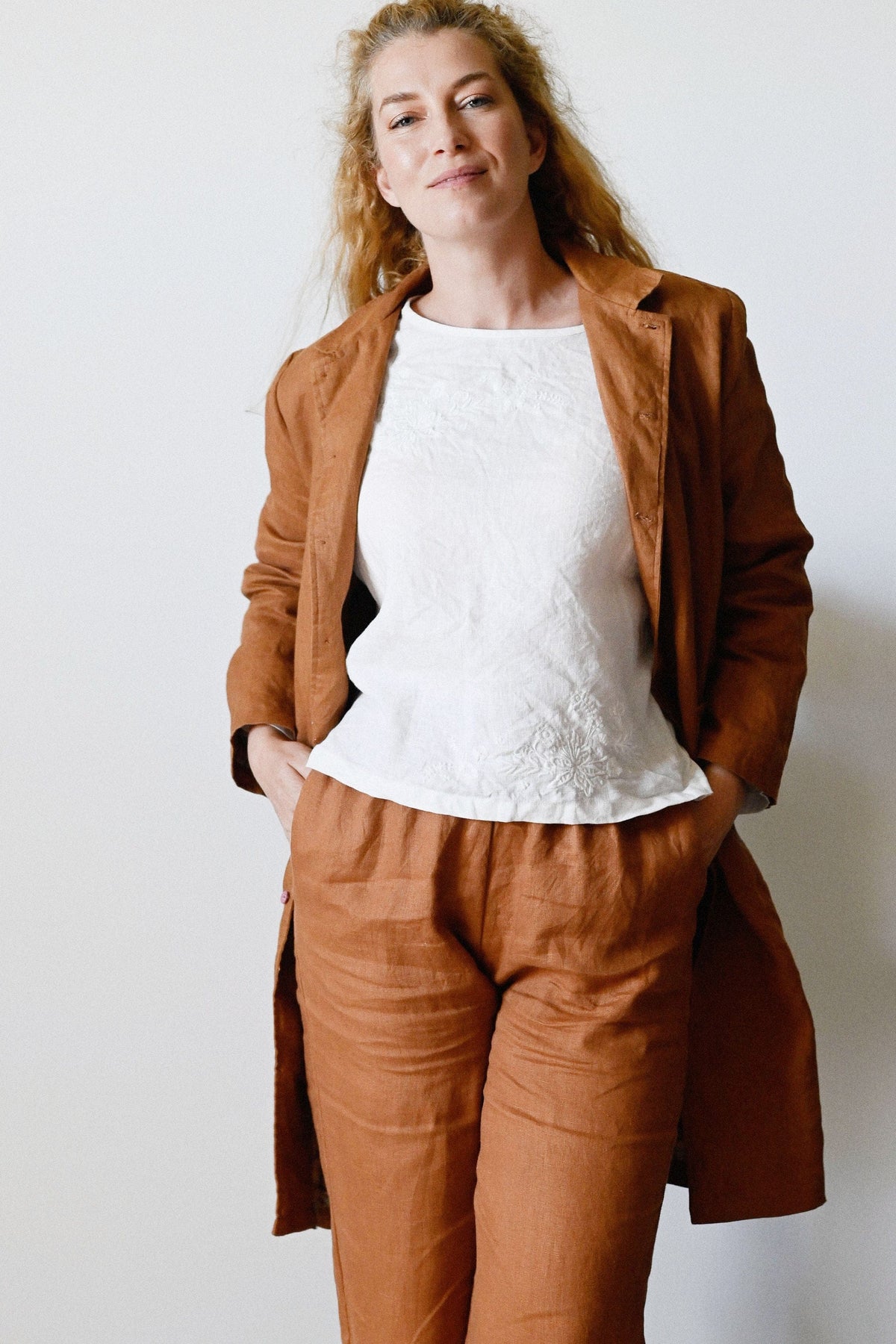 Woman wearing a brown coat and pants with a white top against a plain background