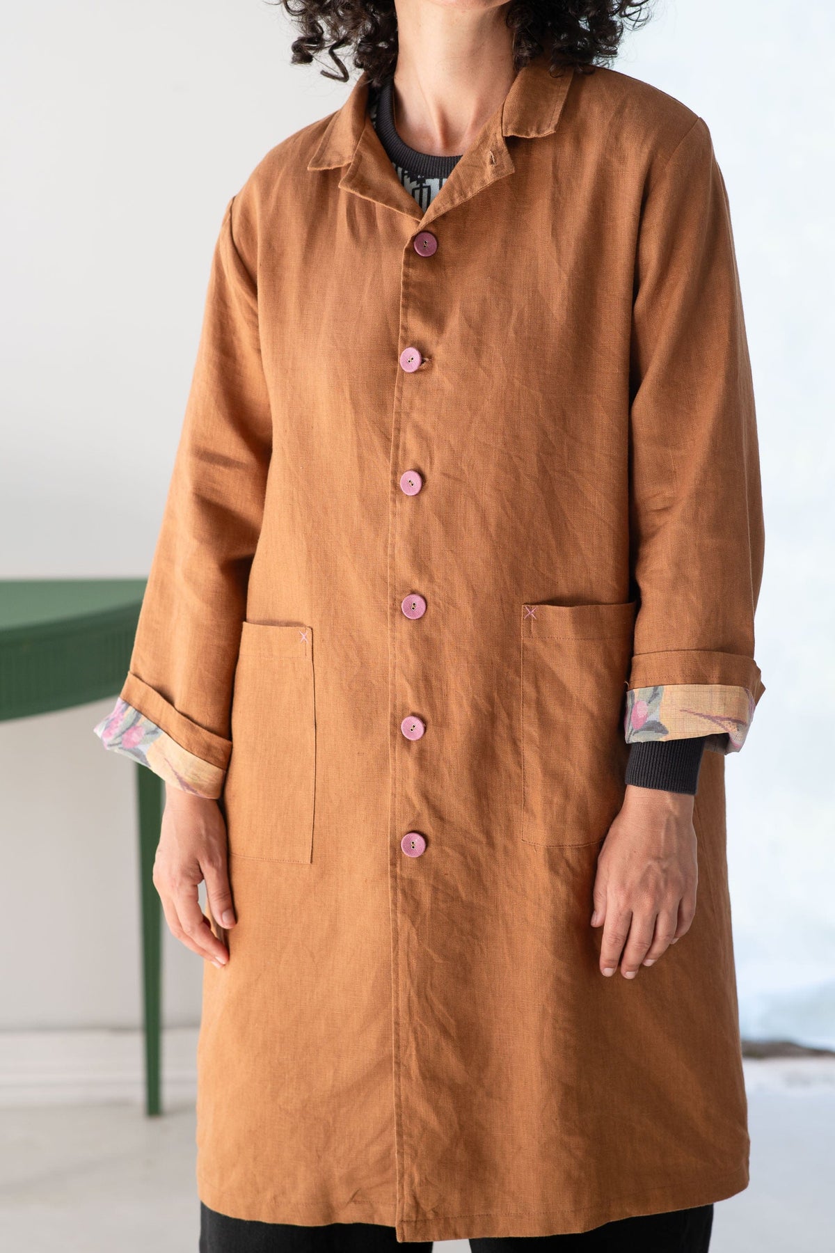 Person wearing a brown coat with pink buttons on a white background